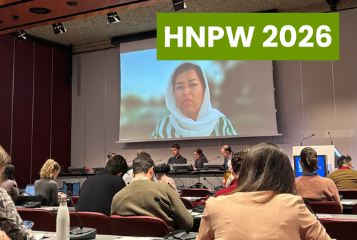 Salle de personne assistant à un débat, un grand écran au milieu est visible avec le visage d'une femme asiatique voilée