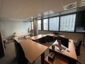 Office with desks, chairs, and a sofa near windows.