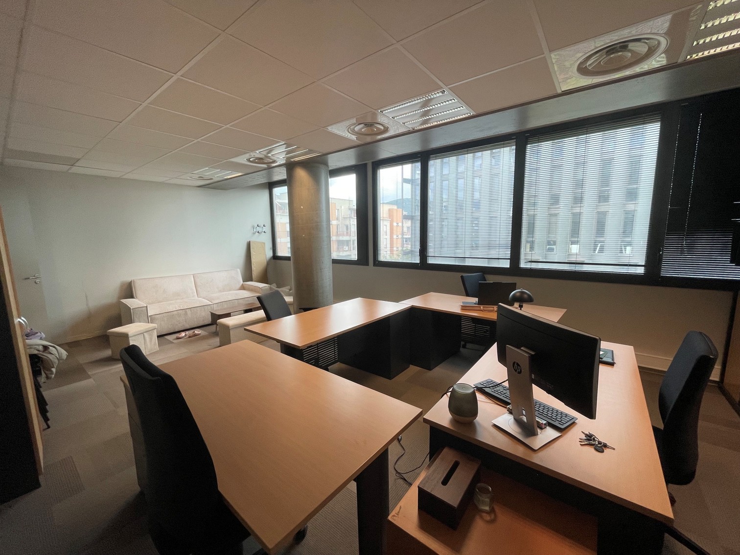 Office with desks, chairs, and a sofa near windows.
