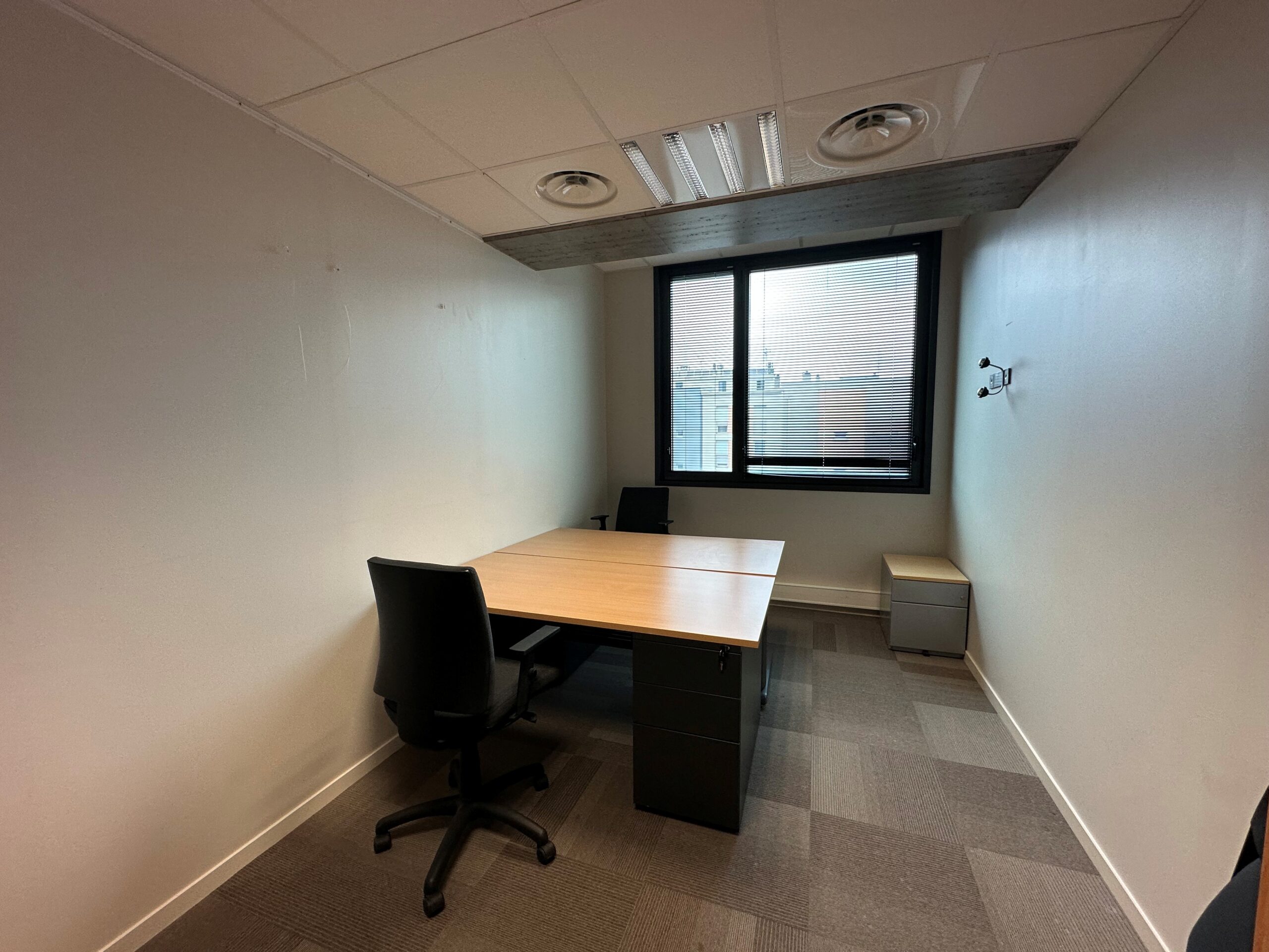 Office room with two desks, chairs, and a window overlooking a city.