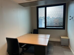 Office with two desks, chairs, and a window overlooking buildings.