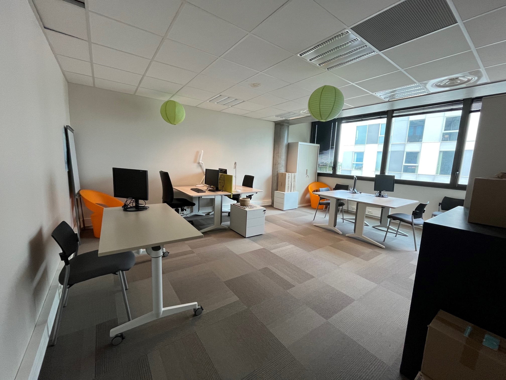 Modern office with desks, chairs, and computers by a large window.