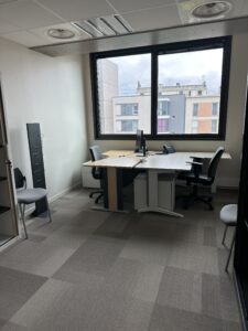 Office with two desks, chairs, and a large window overlooking buildings.