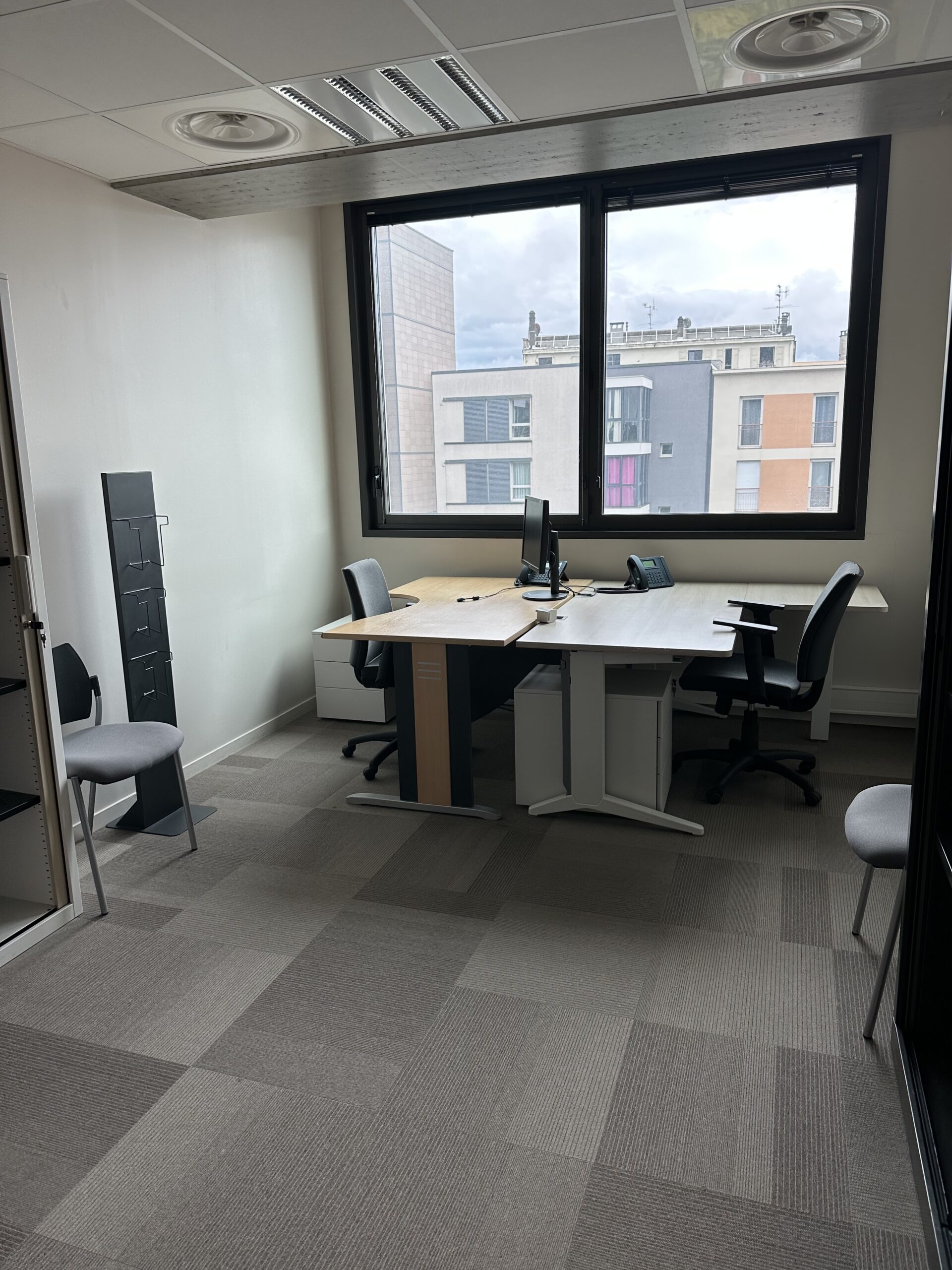 Office with two desks, chairs, and a large window overlooking buildings.