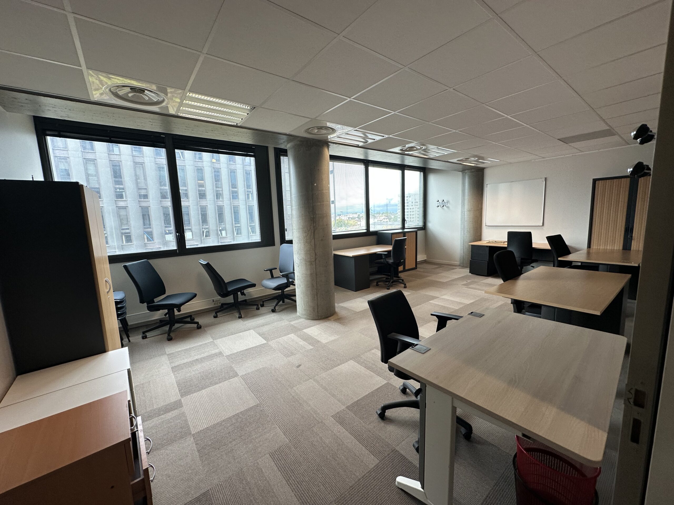 Modern office space with desks, chairs, and large windows overlooking a city.